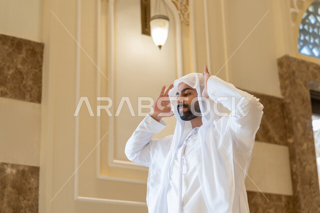 ايماءات التكبير لبدء الصلاة، أداء الفرائض بأوقاتها، رجل عربي خليجي اماراتي يرتدي الكندورة والغترة البيضاء يقف على السجادة يقوم بالتكبير لأداء الصلاة، العبادة والتقرب إلى الله، الشعور بالخشوع والطمأنينة