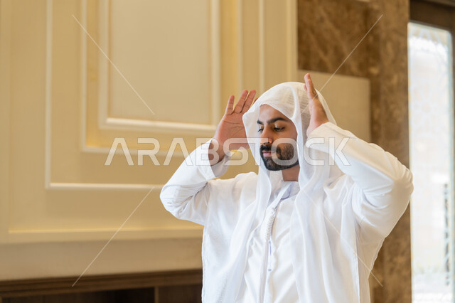 ايماءات التكبير لبدء الصلاة، أداء الفرائض بأوقاتها، رجل عربي خليجي اماراتي يرتدي الكندورة والغترة البيضاء يقف على السجادة يقوم بالتكبير لأداء الصلاة، العبادة والتقرب إلى الله، الشعور بالخشوع والطمأنينة