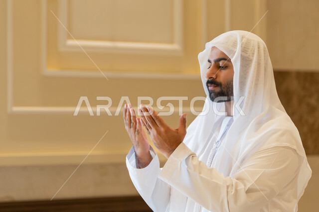 الدعاء و التضرع لرب العباد، أداء فرائض الصلاة بأوقاتها، مفهوم أركان الإسلام، رجل عربي خليجي اماراتي يرتدي الكندورة والغترة البيضاء يقوم بفتح يديه للدعاء والتقرب من الله تعالى، طلب المغفره والعون، الرغبه في تحقيق الأمنيات،