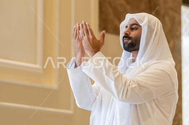 الدعاء و التضرع لرب العباد، أداء فرائض الصلاة بأوقاتها، مفهوم أركان الإسلام، رجل عربي خليجي اماراتي يرتدي الكندورة والغترة البيضاء يقوم بفتح يديه للدعاء والتقرب من الله تعالى، طلب المغفره والعون، الرغبه في تحقيق الأمنيات،