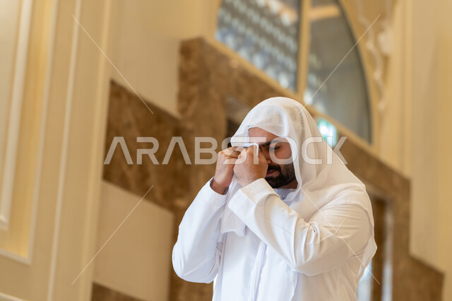 الشعور بالخشوع والطمأنينة, رجل اماراتي عربي خليجي يرتدي الكندورة والغترة البيضاء يقف داخل احدى المساجد في الامارات العربية المتحدة، تعابيرالوجع و البكاء و الخشوع و التضرع لله، التوبة و الرجوع الى الله