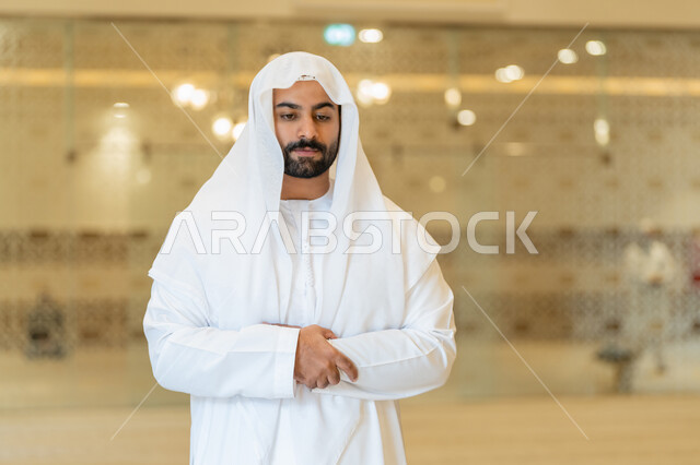 التقرب إلى الله عن طريق القيام بالفرائض والعبادات، الركن الثاني من اركان الاسلام، رجل عربي خليجي اماراتي يرتدي الكندورة والغترة البيضاء يقوم بأداء فريضة الصلاة على وقتها في المسجد، اداء الصلاوات في المساجد
