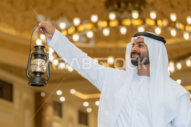 الاستعداد لقدوم شهر رمضان المبارك, التصاميم والديكورات الداخلية للمساجد في الإمارات، العبادة والتقرب إلى الله, أداء الفرائض الدينية, رجل عربي خليجي إماراتي يرتدي الكندورة والغترة البيضاء يقف في المسجد ويمسك بيده فانوس بإيماءات السعادة والسرور