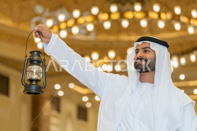 الاستعداد لقدوم شهر رمضان المبارك, التصاميم والديكورات الداخلية للمساجد في الإمارات، العبادة والتقرب إلى الله, أداء الفرائض الدينية, رجل عربي خليجي إماراتي يرتدي الكندورة والغترة البيضاء يقف في المسجد ويمسك بيده فانوس بإيماءات السعادة والسرور