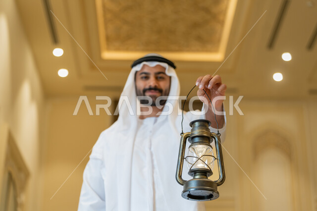الاستعداد لقدوم شهر رمضان المبارك, التصاميم والديكورات الداخلية للمساجد في الإمارات، العبادة والتقرب إلى الله, أداء الفرائض الدينية, رجل عربي خليجي إماراتي يرتدي الكندورة والغترة البيضاء يقف في المسجد ويمسك بيده فانوس بإيماءات السعادة والسرور