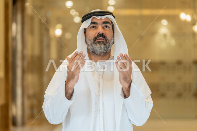 طلب الرحمة والمغفرة,  مفهوم الخشوع والتضرع, العبادة والتقرب الى الله تعالى, رجل عربي خليجي اماراتي يرتدي الكندورة والغترة البيضاء يقف في إحدى المساجد ويرفع يديه للأعلى بتعابير الدعاء, أداء الفرائض الدينية الإسلامية، مفهوم أركان الإسلام