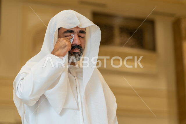 الشعور بالخشوع والطمأنينة, صورة لرجل اماراتي عربي خليجي يرتدي الكندورة والغترة البيضاء يقف داخل احدى المساجد في الامارات العربية المتحدة، تعابير وجع تدل على البكاء و الخشوع و التضرع لله
