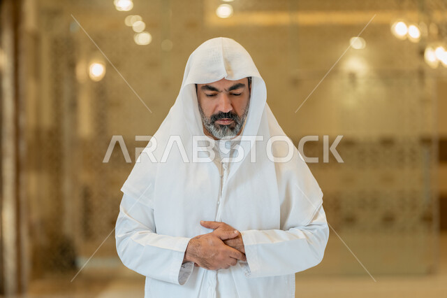 أداء الفرائض الدينية الإسلامية، إقامة الصلاة على وقتها, العبادة والتقرب إلى الله، الركن الثاني من أركان الإسلام، صورة مقربة لرجل عربي خليجي إماراتي يرتدي الكندورة والغترة البيضاء يقف باستقامة, الشعور بالخشوع والطمأنينة