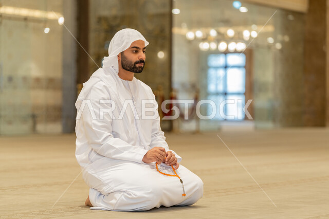 مفهوم التسبيح والتهليل, العبادة والتقرب الى الله تعالى, رجل عربي خليجي إماراتي يرتدي الكندورة والغترة البيضاء يجلس في إحدى المساجد ويمسك بيده سبحة، أداء الفرائض الدينية الإسلامية, أذكار بعد الصلاة، مفهوم التعبد في بيوت الرحمن