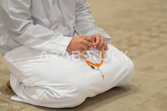 العبادة والتقرب الى الله تعالى, مفهوم التسبيح والتهليل, صورة مقربة  لرجل عربي خليجي إماراتي يرتدي الكندورة والغترة البيضاء يجلس في إحدى المساجد ويمسك بيده سبحة، أداء الفرائض الدينية الإسلامية, أذكار بعد الصلاة، مفهوم التعبد في بيوت الرحمن