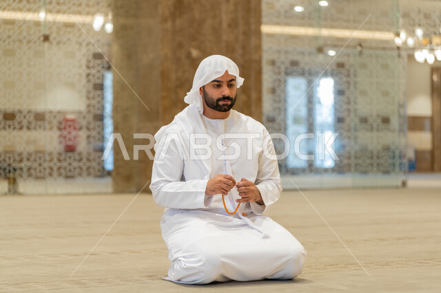 مفهوم التسبيح والتهليل, العبادة والتقرب الى الله تعالى, رجل عربي خليجي إماراتي يرتدي الكندورة والغترة البيضاء يجلس في إحدى المساجد ويمسك بيده سبحة، أداء الفرائض الدينية الإسلامية, أذكار بعد الصلاة، مفهوم التعبد في بيوت الرحمن