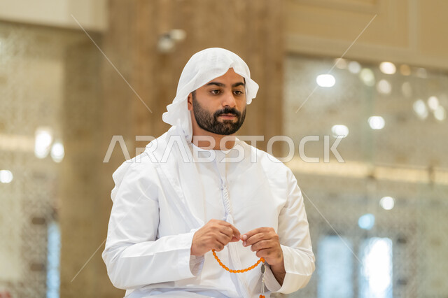 العبادة والتقرب الى الله تعالى, مفهوم التسبيح والتهليل, صورة مقربة  لرجل عربي خليجي إماراتي يرتدي الكندورة والغترة البيضاء يجلس في إحدى المساجد ويمسك بيده سبحة، أداء الفرائض الدينية الإسلامية, أذكار بعد الصلاة، مفهوم التعبد في بيوت الرحمن