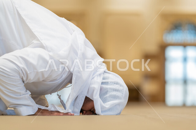 إقامة الصلاة على وقتها, الركن الثاني من أركان الإسلام، الشعور بالخشوع والطمأنينة, أداء الفرائض الدينية الإسلامية، العبادة والتقرب إلى الله، صورة مقربة من الجانب لرجل عربي خليجي إماراتي يرتدي الكندورة والغترة البيضاء يقوم بالسجود في احد المساجد