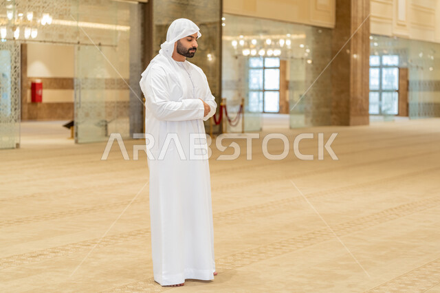 أداء الصلوات على وقتها, الشعور بالخشوع والطمأنينة, الركن الثاني من أركان الإسلام, العبادة والتقرب إلى الله تعالى, القيام بالفرائض الدينية الإسلامية، صورة لرجل عربي خليجي إماراتي يرتدي الكندورة والغترة البيضاء يقف باستقامة واعتدال لأداء فريضة الصلاة