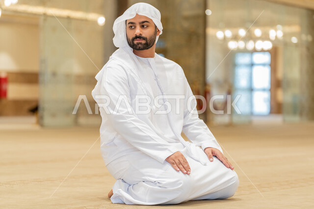مفهوم أركان الإسلام, إقامة الصلاة على وقتها، أداء الفرائض الدينية الإسلامية، رجل عربي خليجي إماراتي يرتدي الكندورة والغترة البيضاء يجلس في المسجد يقوم بالتسليم في ختام صلاته، الشعور بالخشوع والطمأنينة، العبادة والتقرب إلى الله
