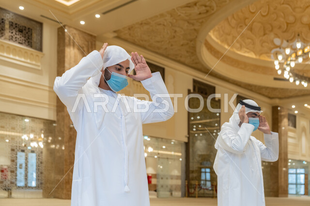الالتزام باجراءات الوقاية، أداء فريضة الصلاه داخل المسجد، صلاة الجماعة لرجلان اماراتيان عربيان خليجيان يرتديان الكندورة والغترة البيضاء ويضعان الكمامة، الحفاظ على التباعد، العبادة و التقرب الى الله