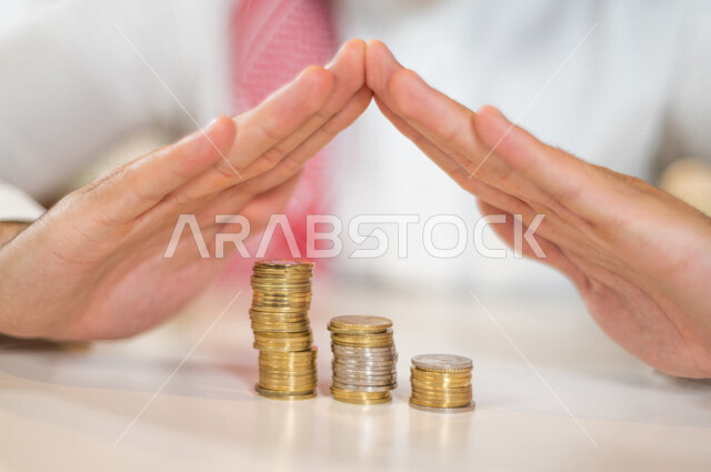 صورة مقربة لرجل عربي خليجي، يحمي العملات المعدنية، النمو والأرباح المالية، إدخار وتوفير الاموال، العملات المعدنية