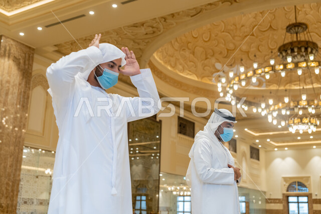 الالتزام باجراءات الوقاية، أداء فريضة الصلاه داخل المسجد، صلاة الجماعة لرجلان اماراتيان عربيان خليجيان يرتديان الكندورة والغترة البيضاء ويضعان الكمامة، الحفاظ على التباعد، العبادة و التقرب الى الله