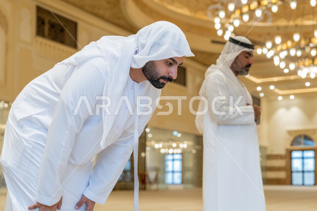 الركن الثاني من أركان الإسلام، إقامة الصلاة على وقتها, أداء الفرائض الدينية الإسلامية، العبادة والتقرب إلى الله، رجلان عربيان خليجيان إماراتيان يرتديان الكندورة والغترة البيضاء يقومان بالصلاة في احد المساجد, الشعور بالخشوع والطمأنينة