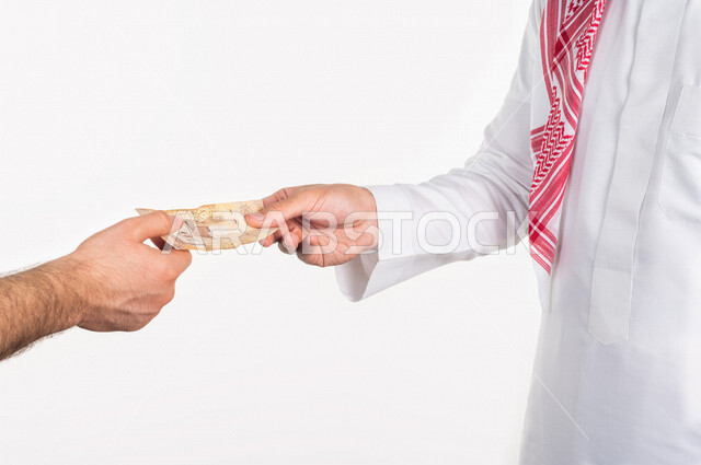Portrait of a Saudi Arabian Gulf man receiving a sum of money from the hand of another person, paper currency for the Saudi riyal, the concept of business financing, saving and saving money, paper money