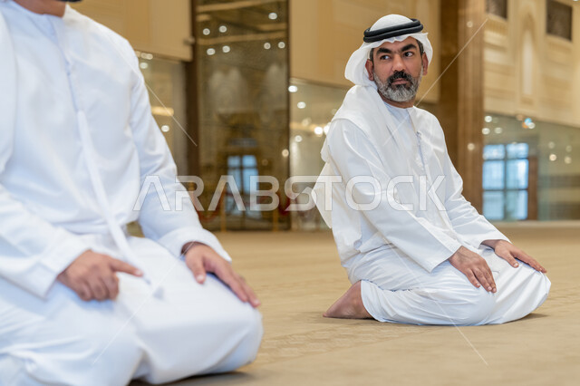 مفهوم أركان الإسلام, إقامة الصلاة على وقتها، أداء الفرائض الدينية الإسلامية، رجلان عرب خليجيان إماراتيان يرتدون الكندورة والغترة البيضاء يجلسون في المسجد يقوم بالتسليم في ختام صلاته، الشعور بالخشوع والطمأنينة، العبادة والتقرب إلى الله