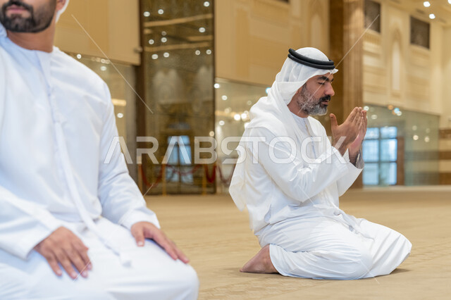 الجلوس للدعاء والاستغفار في احد المساجد بالامارات العربية المتحدة, رجلان عربيان اماراتيان خليجيان يرتديان الكندورة والغترة البيضاء يؤدي فريضة الصلاة، الخشوع والتضرع للرحمن، التقرب الى الله بأداء العبادات