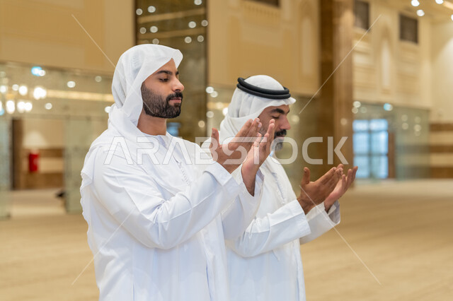 الدعاء و التضرع لرب العباد، أداء فرائض الصلاة بأوقاتها، مفهوم أركان الإسلام، رجلان عربيان خليجيان اماراتيان يرتدون الكندورة والغترة البيضاء يقفون على السجادة بأيادي مفتوحة للأعلى، العبادة والتقرب إلى الله،