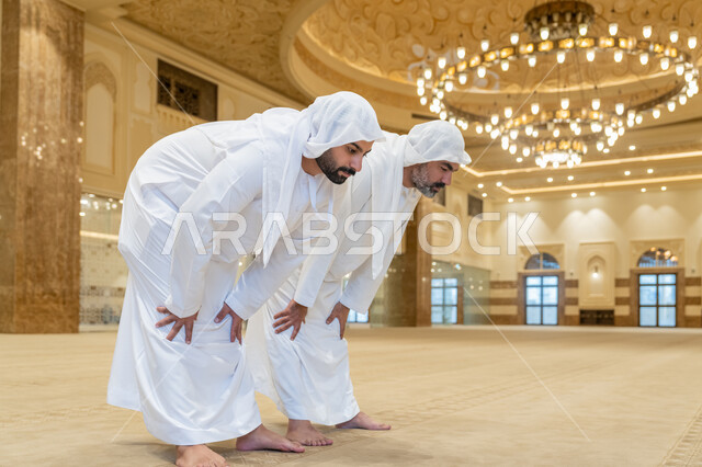 الركن الثاني من أركان الإسلام، إقامة الصلاة على وقتها, أداء الفرائض الدينية الإسلامية، العبادة والتقرب إلى الله، صورة مقربة لرجلين عربيين خليجيين إماراتيين يرتديين الكندورة والغترة البيضاء يقومان بالركوع, الشعور بالخشوع والطمأنينة