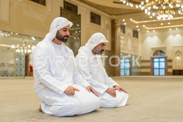 الجلوس للتشهد في احد المساجد بالامارات العربية المتحدة, رجلان عربيان اماراتيان خليجيان يرتديان الكندورة والغترة البيضاء يؤدي فريضة الصلاة، الخشوع والتضرع للرحمن، التقرب الى الله بأداء العبادات