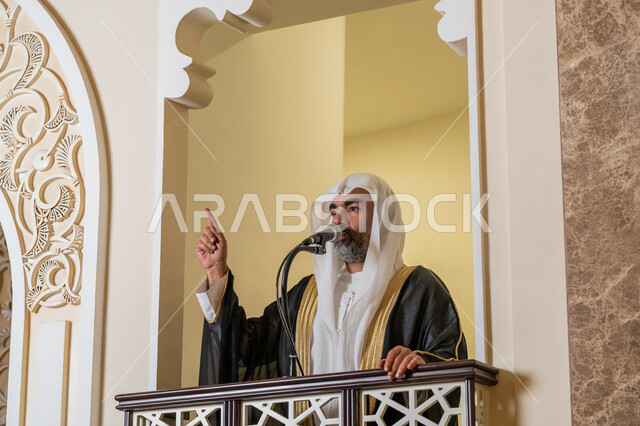 مفهوم العبادة والتقرب إلى الله تعالى, توجيه الناس نحو الحق والهداية, دور أئمة المساجد والخطباء في نشر الدين، إمام عربي خليجي إماراتي يرتدي البشت والكندورة والغترة البيضاء يقف أمام مكبر الصوت ويلقي الخطبة على المنبر, نداء المسلمين لأداء الفرائض