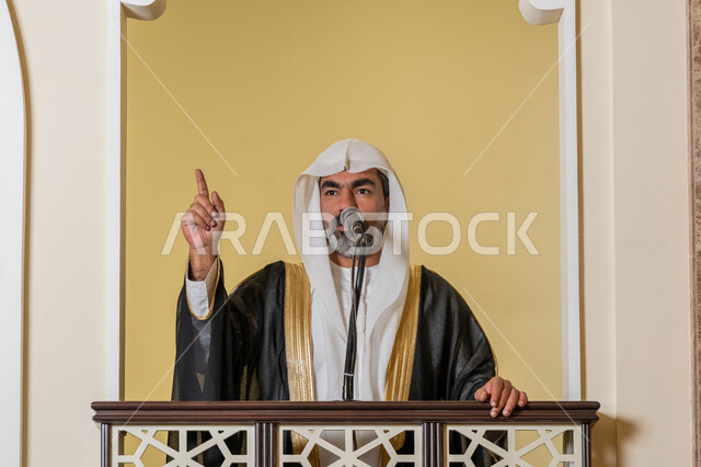 توجيه الناس نحو الحق والهداية, مفهوم العبادة والتقرب إلى الله تعالى, دور أئمة المساجد والخطباء في نشر الدين، إمام عربي خليجي إماراتي يرتدي البشت والكندورة والغترة البيضاء يقف أمام مكبر الصوت ويلقي الخطبة على المنبر, نداء المسلمين لأداء الفرائض