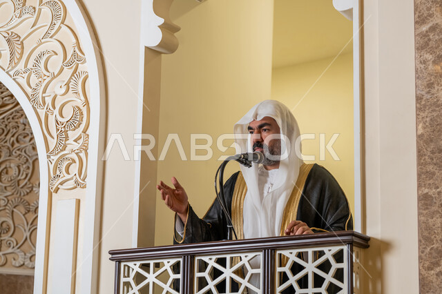 توجيه الناس نحو الحق والهداية, مفهوم العبادة والتقرب إلى الله تعالى, دور أئمة المساجد والخطباء في نشر الدين، إمام عربي خليجي إماراتي يرتدي البشت والكندورة والغترة البيضاء يقف أمام مكبر الصوت ويلقي الخطبة على المنبر, نداء المسلمين لأداء الفرائض