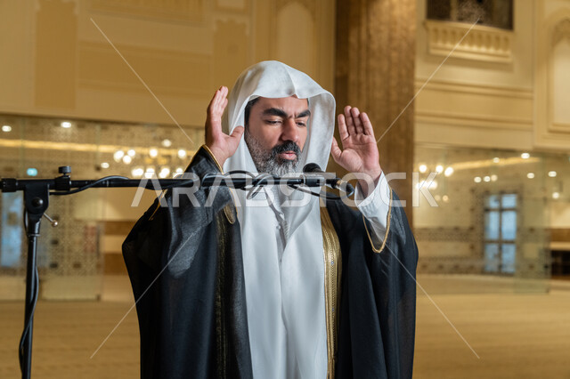 الركن الثاني من أركان الإسلام, الشعور بالخشوع والطمأنينة, أداء فرائض الدين الإسلامي, إمامة المسلمين في المسجد, إقامة الصلاة على وقتها، صورة مقربة لإمام عربي خليجي إماراتي يرتدي البشت والكندورة والغترة البيضاء يقوم بأداء فريضة الصلاة ويرفع يديه لتكبيرة الإحرام