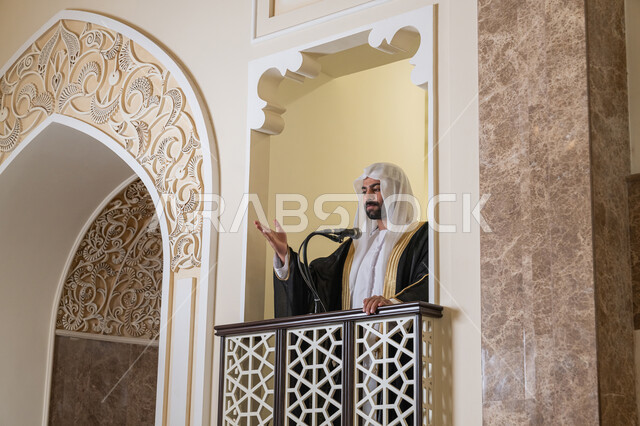 مفهوم العبادة والتقرب إلى الله تعالى, توجيه الناس نحو الحق والهداية, دور أئمة المساجد والخطباء في نشر الدين، إمام عربي خليجي إماراتي يرتدي البشت والكندورة والغترة البيضاء يقف أمام مكبر الصوت ويلقي الخطبة على المنبر, نداء المسلمين لأداء الفرائض