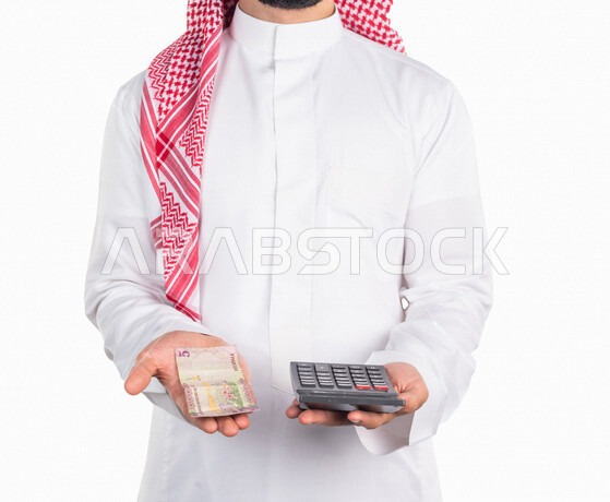 بورتريه لرجل عربي خليجي سعودي، يحمل في يده عملة ورقية والة حاسبة في اليد الاخرى، العملات الورقية للريال السعودية، استخدام الالة الحاسبة لاجراء العمليات الحسابية، ادارة الحسابات