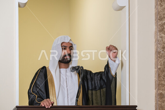 مفهوم العبادة والتقرب إلى الله تعالى, توجيه الناس نحو الحق والهداية, دور أئمة المساجد والخطباء في نشر الدين، إمام عربي خليجي إماراتي يرتدي البشت والكندورة والغترة البيضاء يقف أمام مكبر الصوت ويلقي الخطبة على المنبر, نداء المسلمين لأداء الفرائض