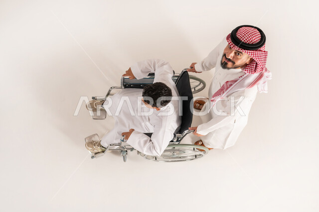 Family support and encouragement for people with disabilities, improving the lives of people with mobility disabilities, vertical top portrait of a Saudi Arabian Gulf man wearing traditional thobe helping his son with special needs, white background