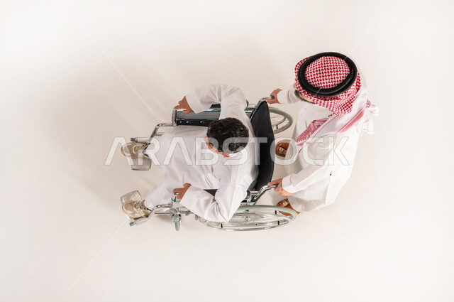 تحسين حياة ذوي الإعاقة الحركية على التنقل, الدعم والتشجيع العائلي لأصحاب الهمم, بورتريه علوي عامودي لرجل عربي خليجي سعودي يرتدي الثوب التقليدي يقوم بمساعدة ابنه من ذوي الاحتياجات الخاصة، خلفية بيضاء