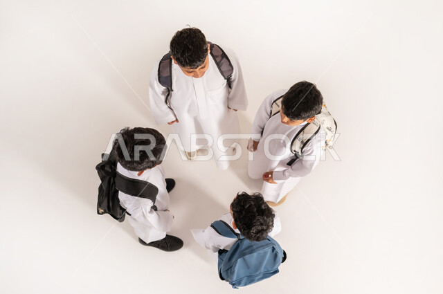 موسم العودة للمدارس في السعودية, الاستعداد للعام الدراسي الجديد, بورتريه علوي عامودي لأولاد عربيين خليجيين سعوديين يرتدون الثوب التقليدي يقفون باستقامة ويحملون الحقائب على ظهرهم, خلفية بيضاء