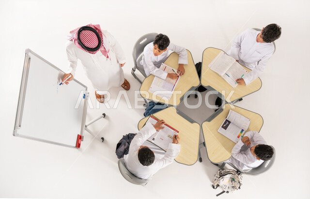 المثابرة على الدراسة لتحقيق النجاح، اكتساب المعرفة و الخبرات العلمية، بورتريه علوي عامودي لمعلم عربي خليجي سعودي يقوم بإعطاء الدروس، تلاميذ عرب خليجيون سعوديون يرتدون الثوب السعودي التقليدي يجلسون بشكل مجموعة، الجلسات والحصص التعليمية، خلفية بيضاء