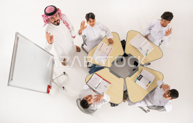 Educational sessions and classes, looking at the camera with gestures of enthusiasm and happiness, vertical overhead portrait of a Saudi Arabian Gulf teacher giving lessons, Saudi Arabian Gulf students wearing traditional Saudi thobe sitting in a group, perseverance in studying to achieve success, white background