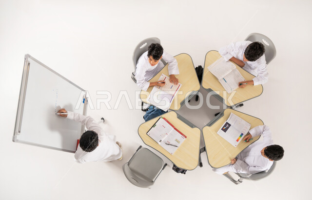 التعليم الدراسي في السعودية، بورتريه علوي عامودي لتلاميذ عرب خليجيون سعوديون يرتدون الثوب السعودي التقليدي ينظرون الى صديقهم وهو يشرح فكرة ما، تأدية الواجبات المدرسية، الاهتمام بالعلم والتعلم، مفهوم الاجتهاد و طلب التفوق، خلفية بيضاء