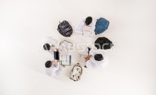 عرض شاشة سوداء فارغة، كتابة الواجبات المنزلية، تنمية المهارات الابداعية، بورتريه علوي عامودي لمجموعة أولاد عربيين خليجيين سعوديين يرتدون الثوب التقليدي يجلسون على الأرض, الاستمتاع بالأنشطة الترفيهية الجماعية,  استخدام التقنيات الحديثة في التعليم، خلفية بيضاء