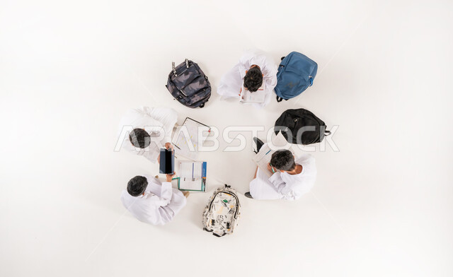 استخدام التقنيات الحديثة في التعليم، عرض شاشة سوداء فارغة، كتابة الواجبات المنزلية، تنمية المهارات الابداعية، بورتريه علوي عامودي لمجموعة أولاد عربيين خليجيين سعوديين يرتدون الثوب التقليدي يجلسون على الأرض, الاستمتاع بالأنشطة الترفيهية الجماعية, خلفية بيضاء