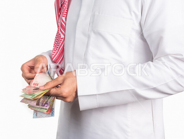 بورتريه لرجل عربي خليجي يحمل بيده كومة من العملات الورقية، النمو والأرباح المالية، إدخار وتوفير الاموال، عملات نقدية ورقية للريال السعودي