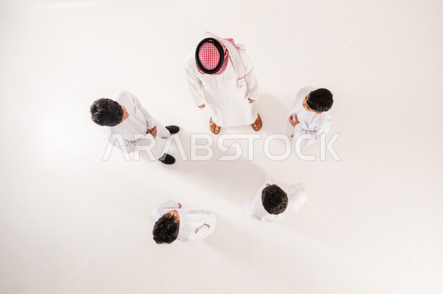 الانسجام والمودة بين افراد الاسرة، مساندة الأبناء و تشجيعهم، بورتريه علوي عامودي لرجل عربي خليجي سعودي يرتدي الثوب التقليدي والشماغ يقوم بقضاء وقت ممتع مع الاولاد، خلفية بيضاء