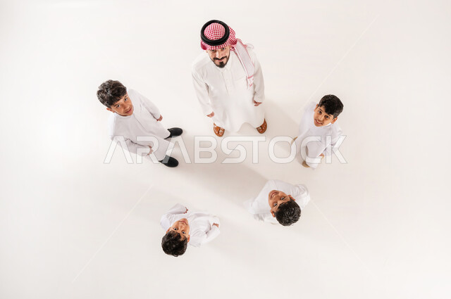 الالفة والانسجام والمودة بين افراد الاسرة،  قضاء وقت ممتع مع الاولاد، مساندة الأبناء و تشجيعهم، بورتريه علوي عامودي لرجل عربي خليجي سعودي يرتدي الثوب التقليدي والشماغ يقف برفقة اولاده ينظر الى الكاميرا بايماءات السرور والسعادة، خلفية بيضاء