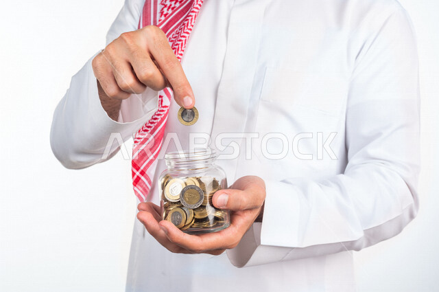 Portrait of a Gulf Arab man, saving and saving money in a glass bowl, financial growth and profits, saving and saving money, coins