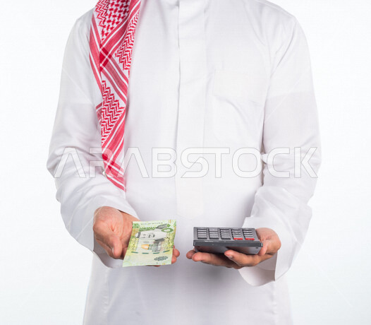 بورتريه لرجل عربي خليجي سعودي، يحمل في يده عملة ورقية والة حاسبة في اليد الاخرى، العملات الورقية للريال السعودية، استخدام الالة الحاسبة لاجراء العمليات الحسابية، ادارة الحسابات