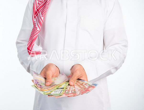 بورتريه لرجل عربي خليجي يحمل بيده كومة من العملات الورقية، النمو والأرباح المالية، إدخار وتوفير الاموال، عملات نقدية ورقية للريال السعودي